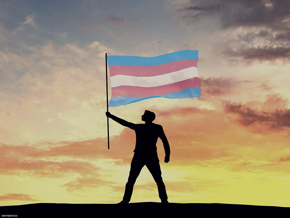 shadow of a person holding the transgender flag against a sunrise