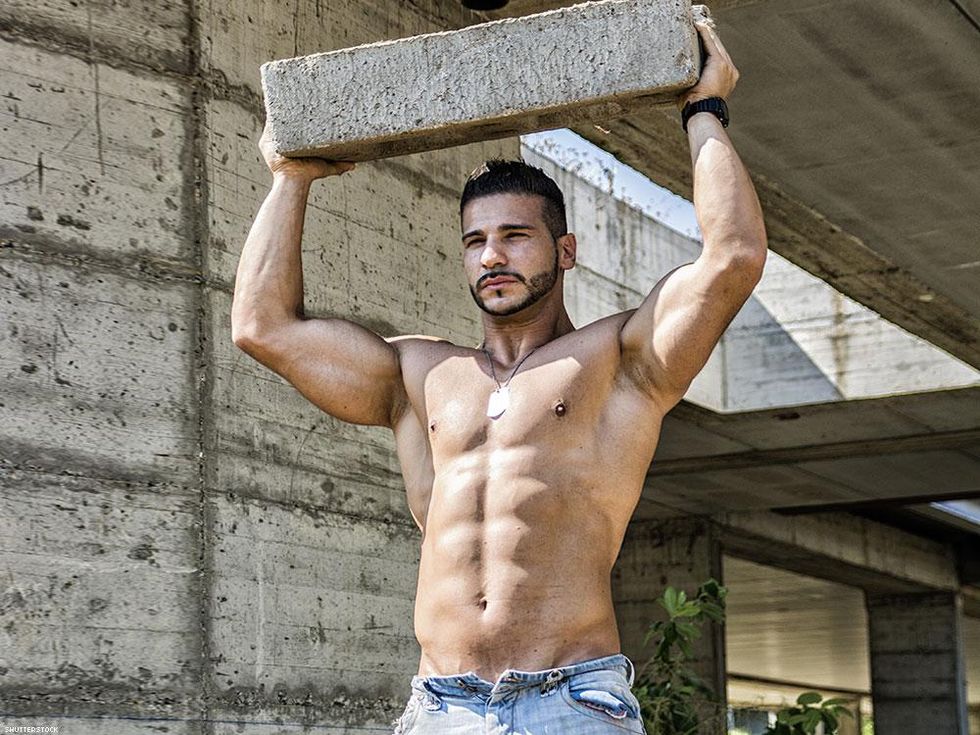 shirtless man in jeans holding cement block