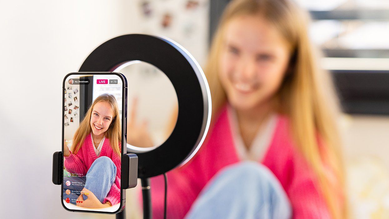 Teenage girl filming herself with mobile phone at home and live streaming on social media