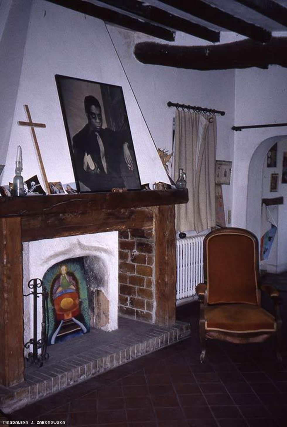The upstairs living room with Baldwin\u2019s portrait, a cross, and mantelpiece collage.