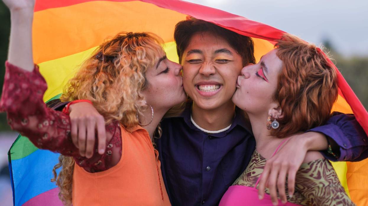 Three people kissing under a rainbow flag