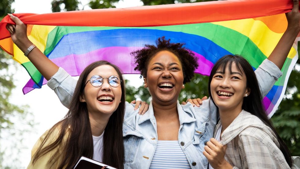 Three women with a rainbow flag over them