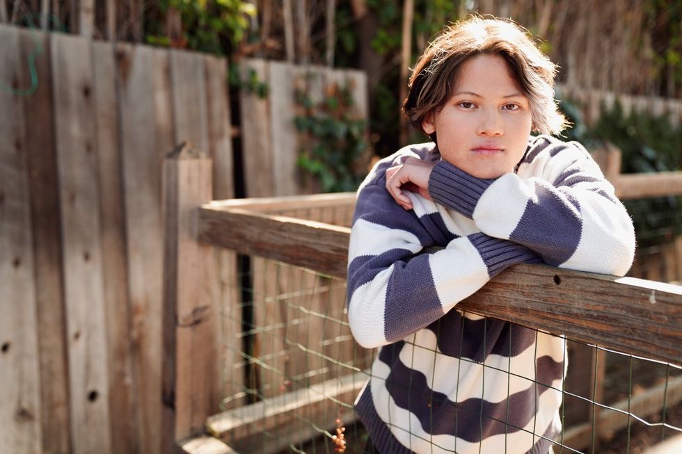 transgender teen Mat leans on wood and wire fence