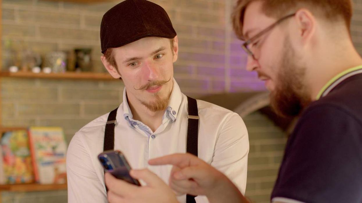 Two male-presenting people looking at a mobile phone