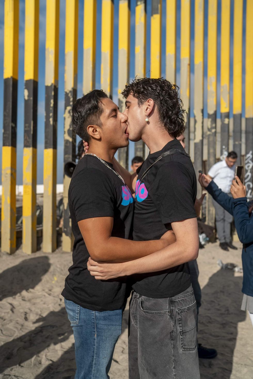 Two men kissing in front of the US-Mexico border