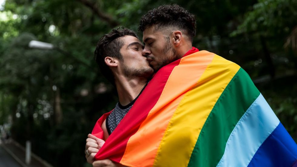 Two men kissing with rainbow flag around them