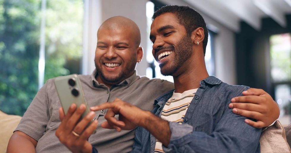 two men seated on a couch look at a smart phone together