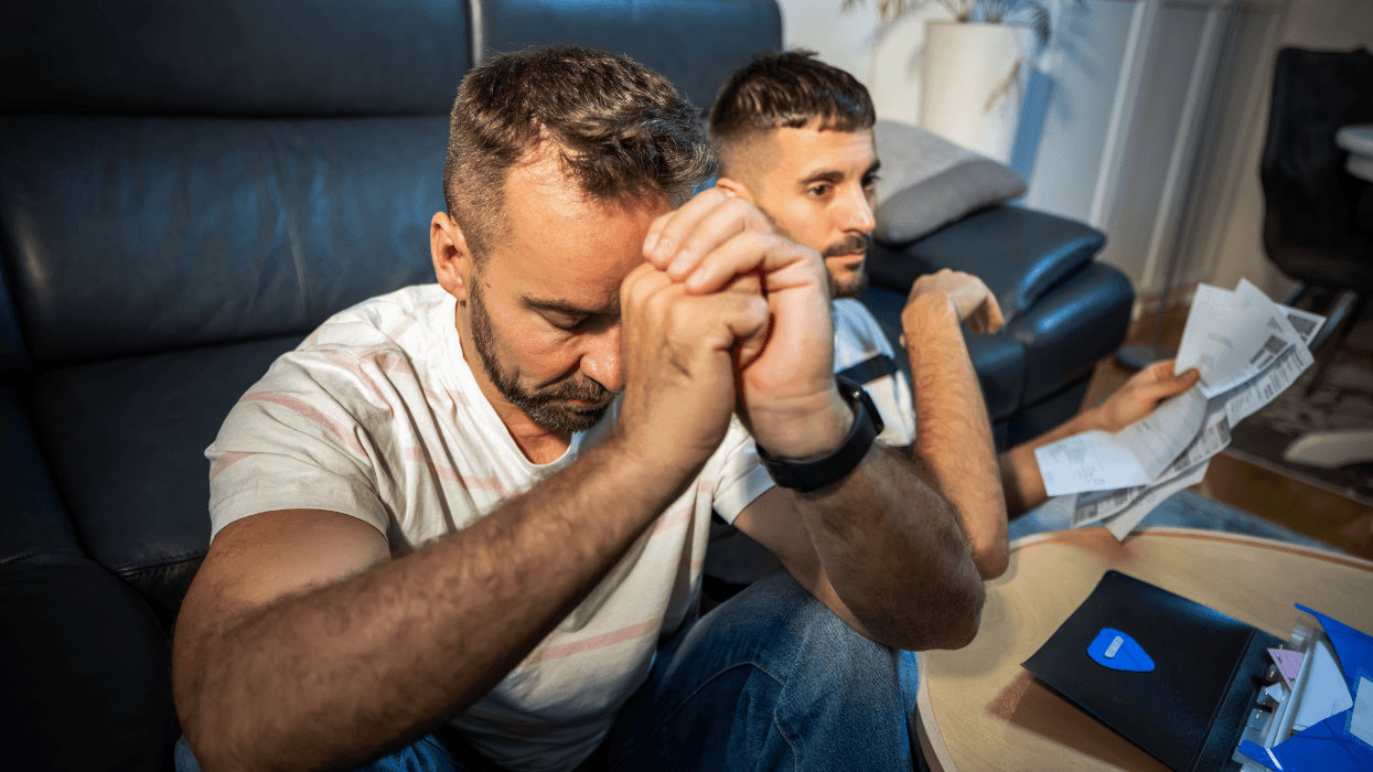 Two men sit together at a coffee table while reviewing documents.