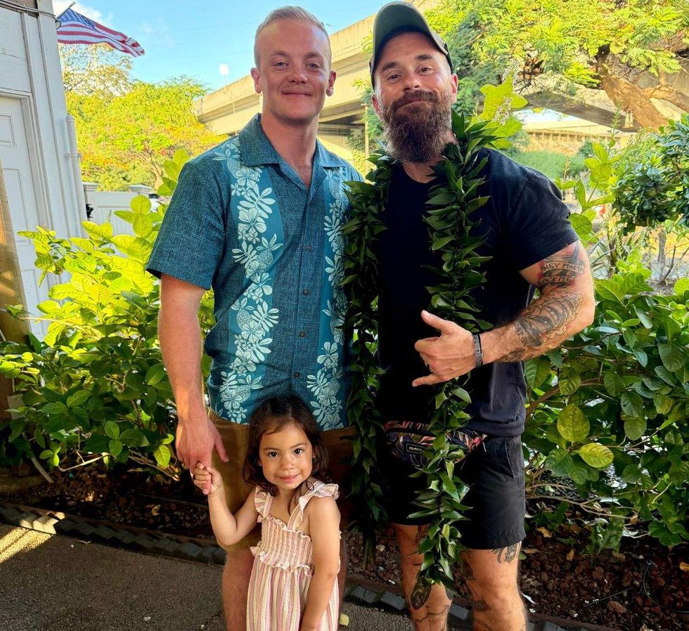 two men standing in front of folliage with a little girl