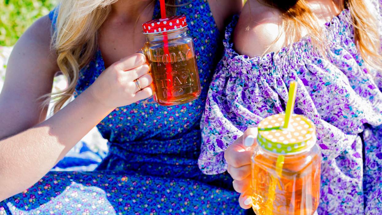 Two people in floral dresses holding mason jar drinks with straws outdoors.