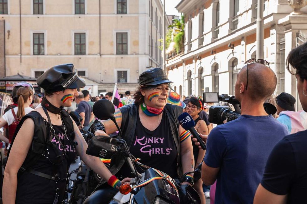 two people in leather biker attire speak to a journalist at an lgbtq event