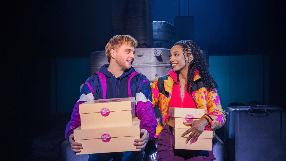 Two people sitting on top of suitcases, holding cake boxes and looking at each other.