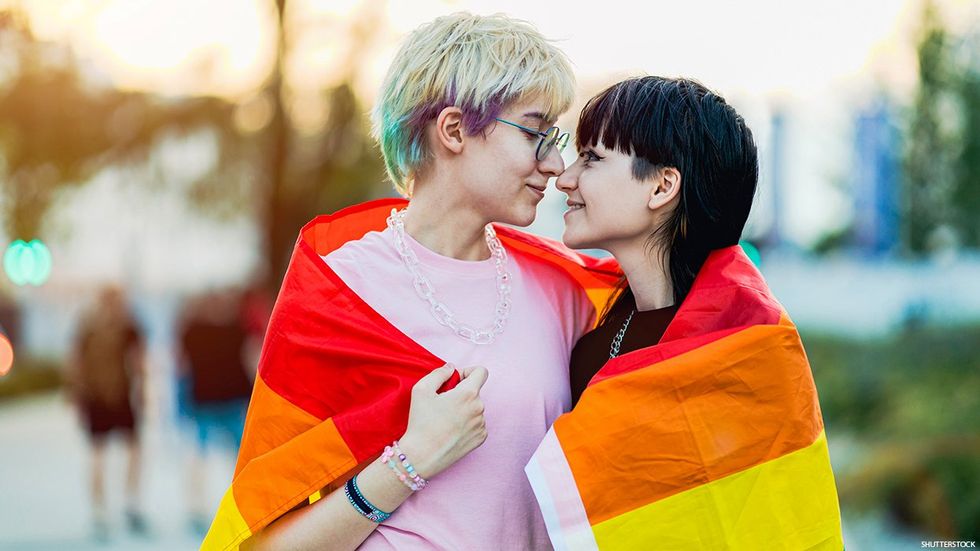 Two people wrapped in a rainbow flag.