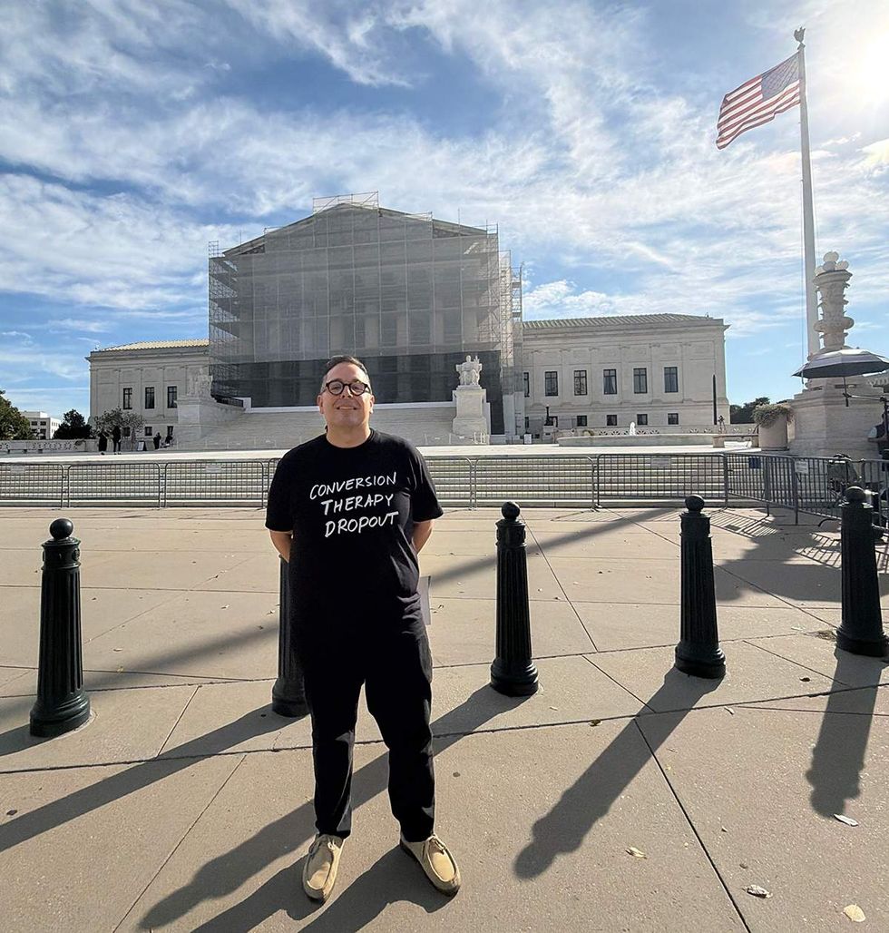 \u200bTimothy Schraeder Rodriguez in conversion therapy dropout tshirt in front of US Supreme Court building with american flag waving