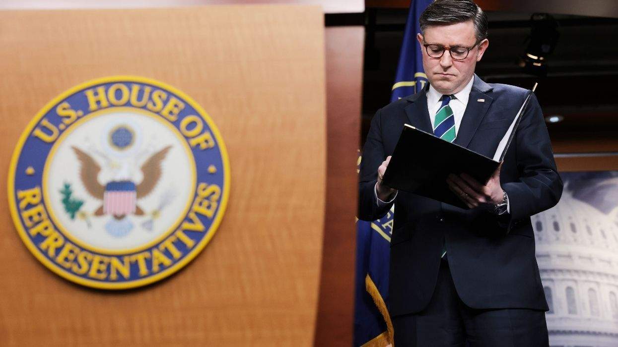 us house speaker mike johnson next to a house of representatives lectern while looking at a folder