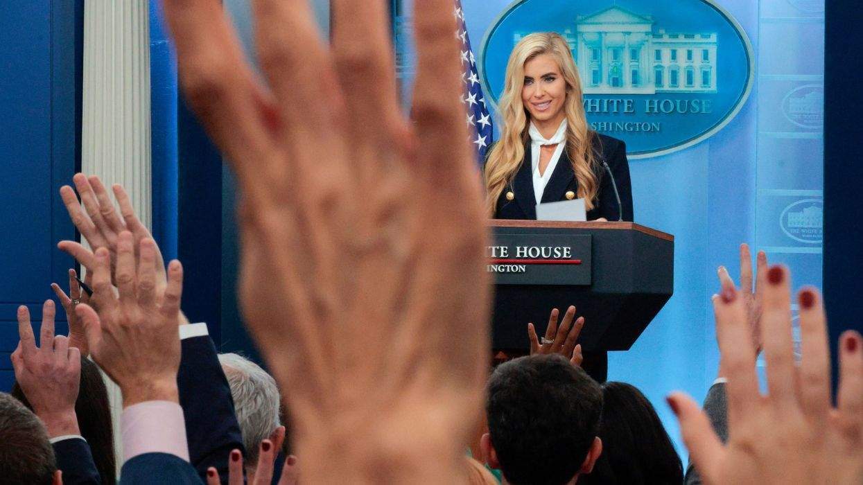 white house press secretary katie zacharia looks out onto a room of raised hands by reporters