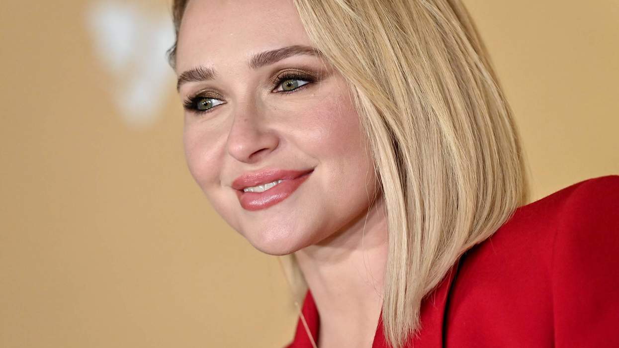 Woman in a red blazer with blonde bob haircut, smiling against a beige background.