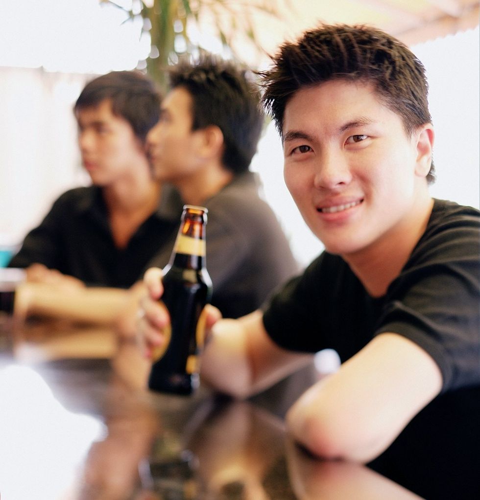 Young man at Singapore bar counter holding beer bottle gay couple in the background