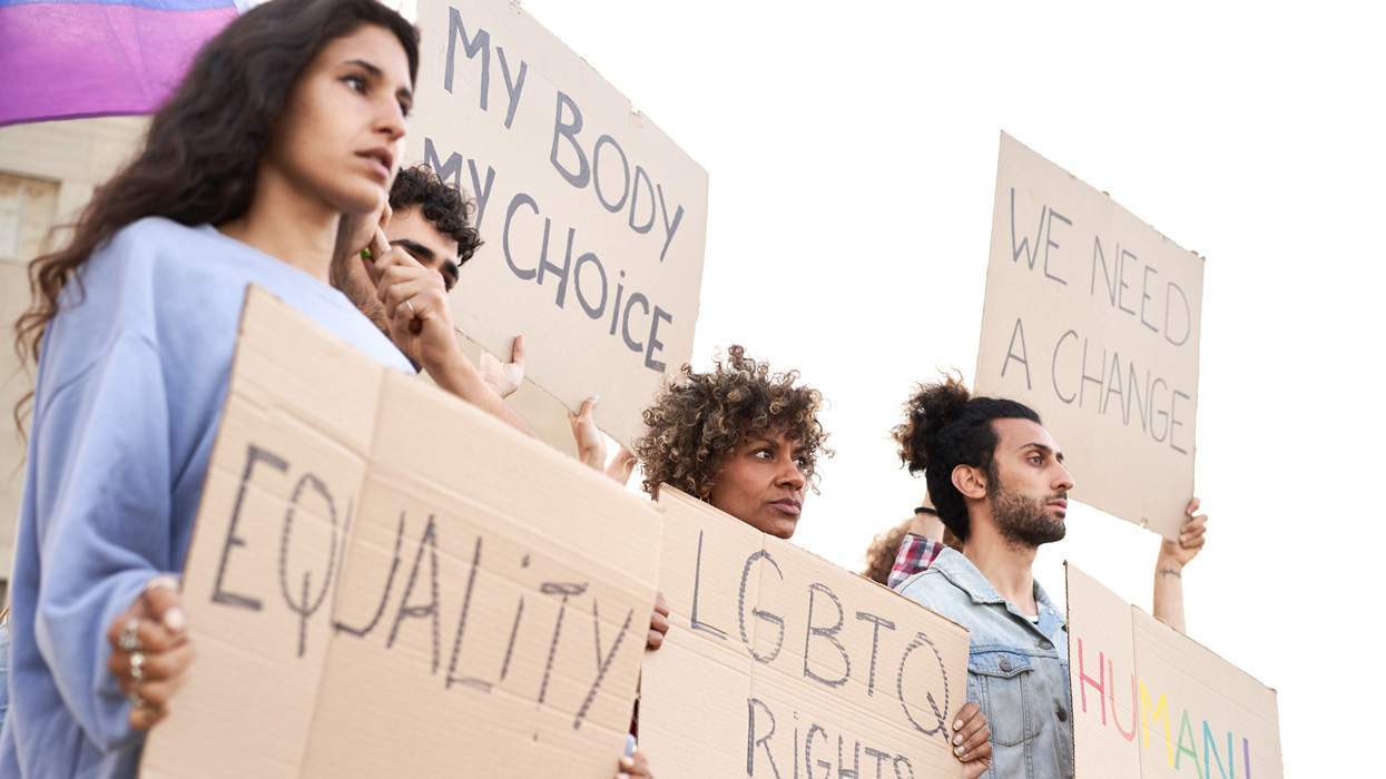 young people hold protest signs with messages of lgbtq rights