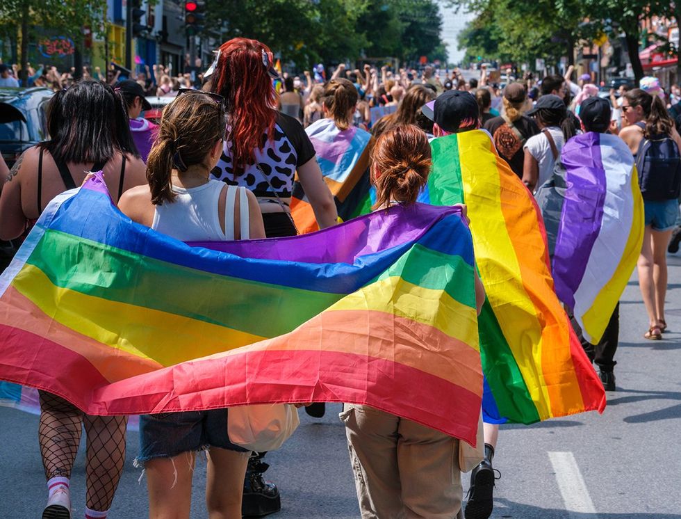 young queer nonbinary group marching in LGBTQIA pride parade with rainbow flag capes