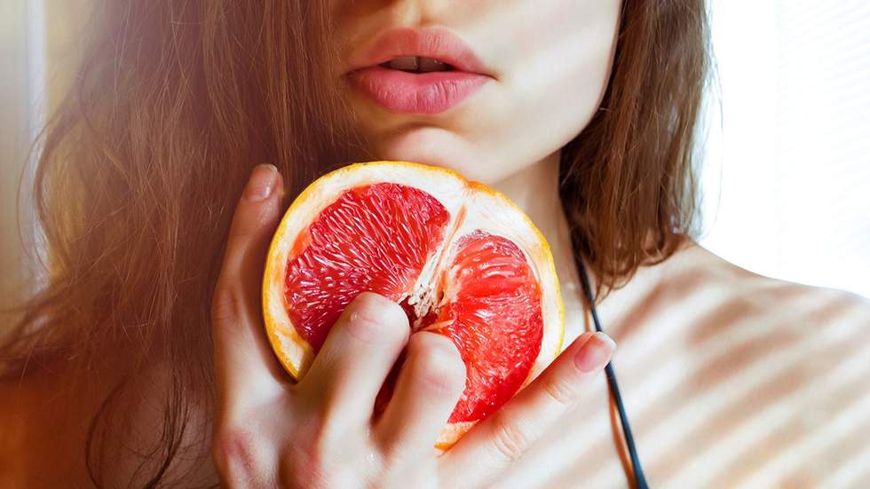 young woman holding two fingers on grapefruit