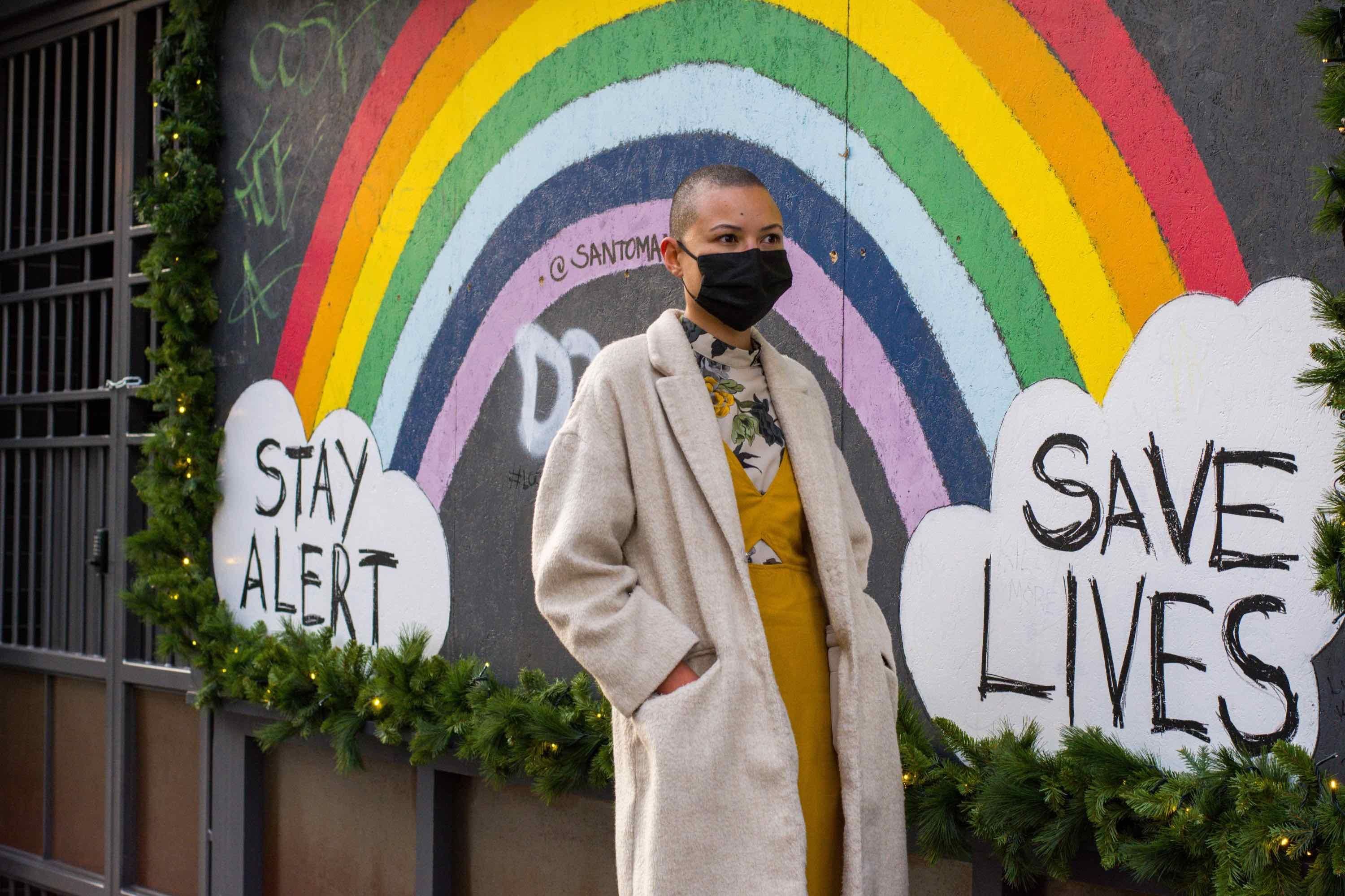 rainbow stay alert save lives poster behind a woman in a mask