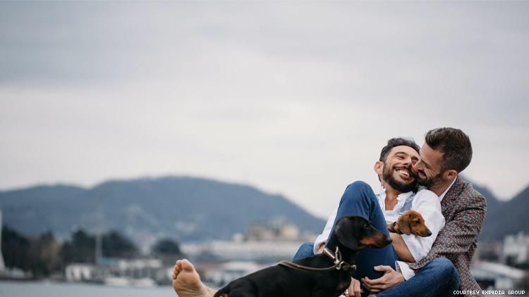 Gay male couple with two dogs relax in front of a lake and mountains