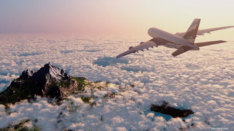 Airplane soars above the clouds and a mountain peak