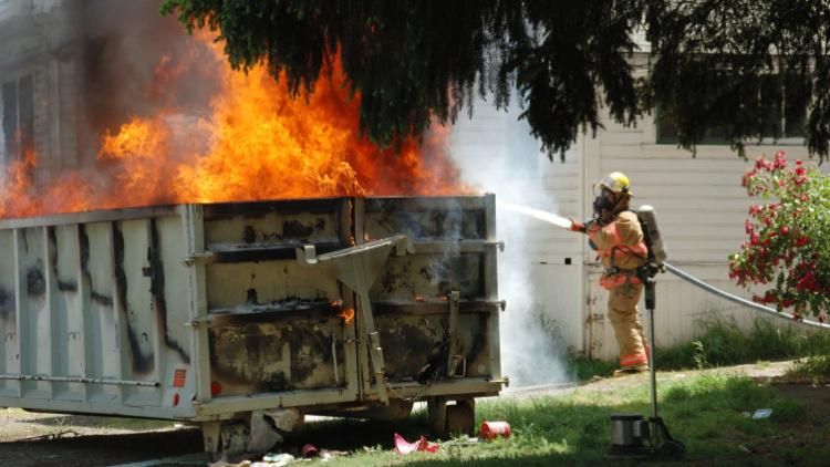Dumpster on fire with firefighter trying to put it out
